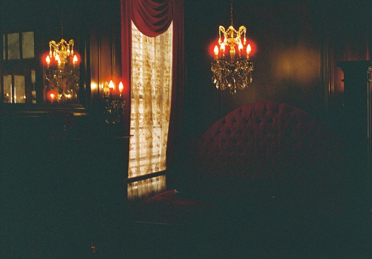 Red velvet furniture and curtains beneath chandeliers in a wood-paneled room at South Eden Plantation, photographed on film.