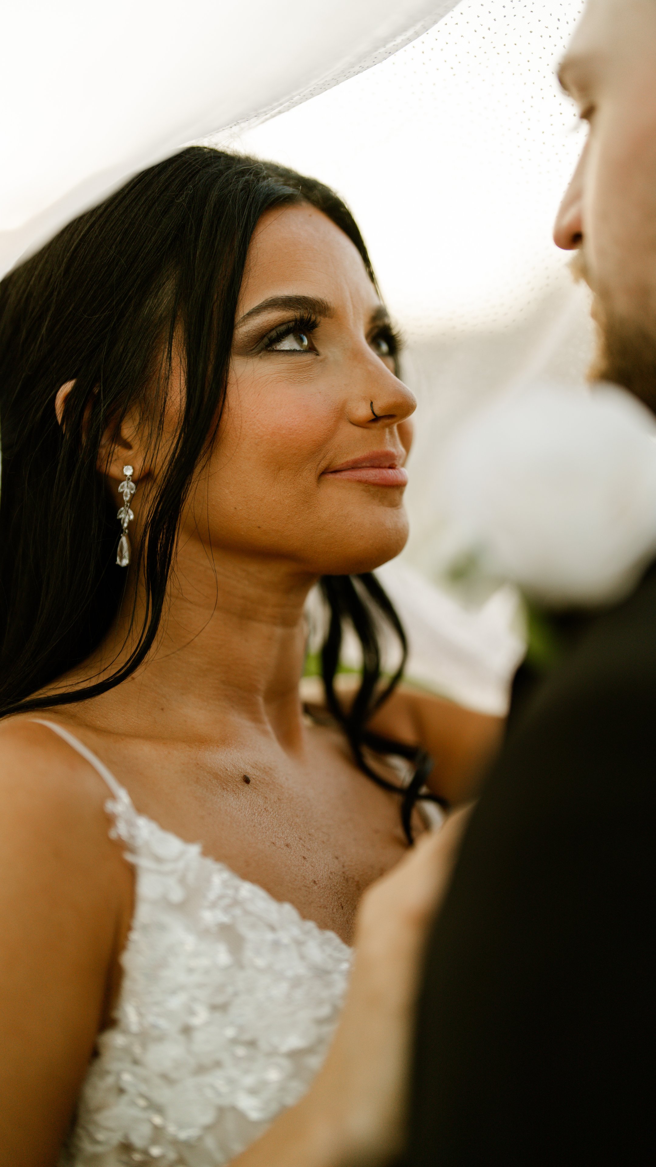 A close view of Kenadee in her dress and earrings, smiling, with Corey's shoulder in the frame.