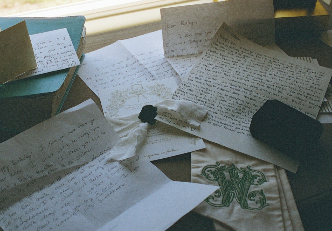 Handwritten letters, wedding stationery and monogrammed fabric beside the window at Raley and Drew’s wedding, photographed on film.