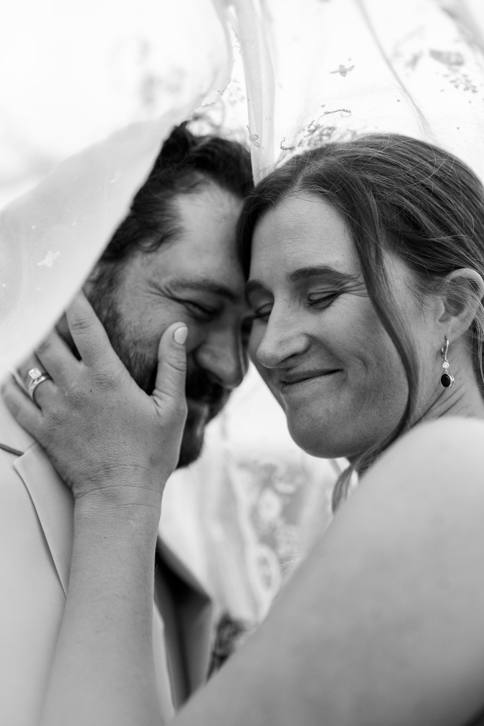 In black and white, Elizabeth smiles with her eyes closed beneath her veil, her ringed hand on Dustin's cheek.