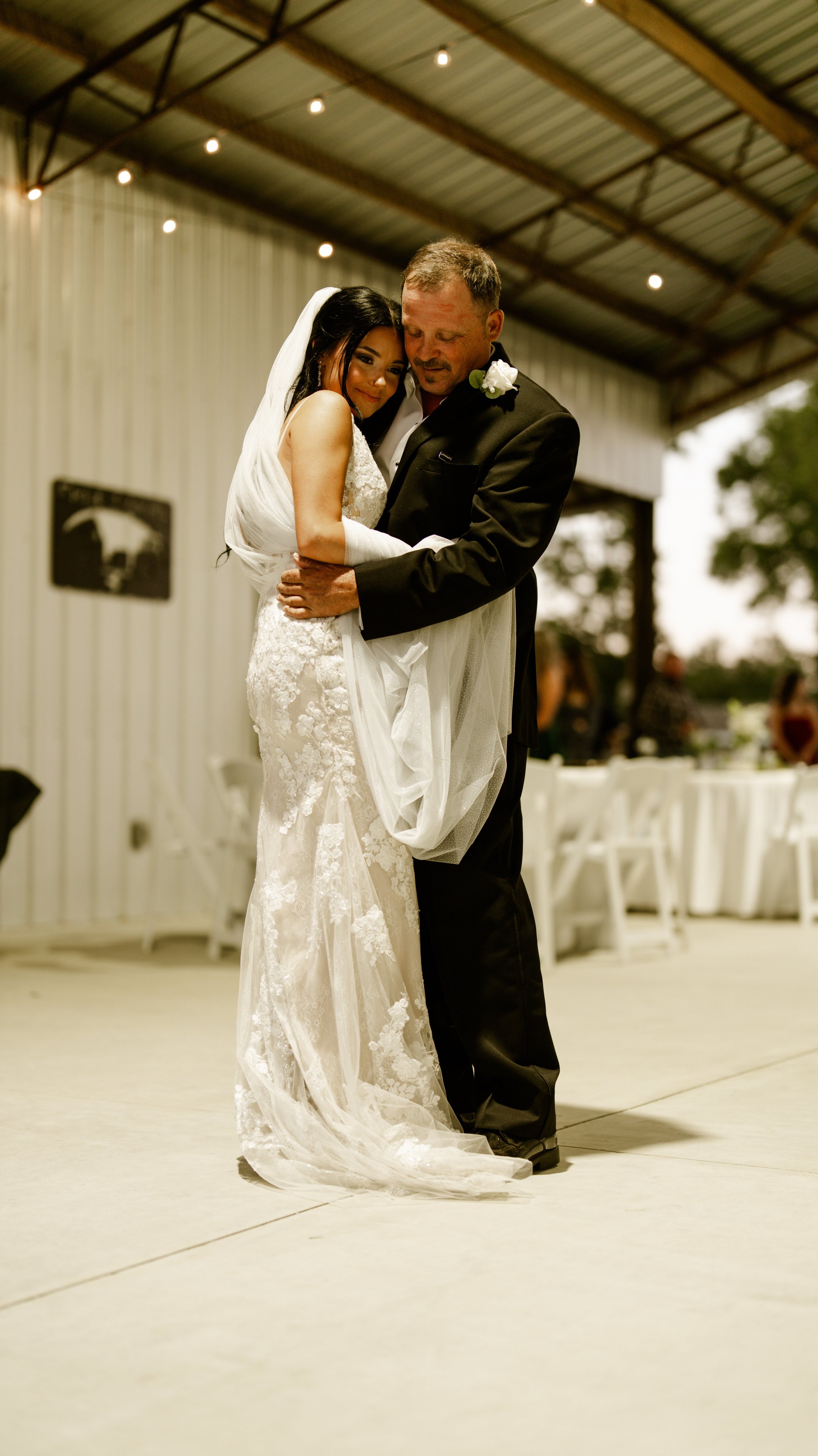 Kenadee dancing with a man in a dark suit on a pale floor under a string-lit pavilion.