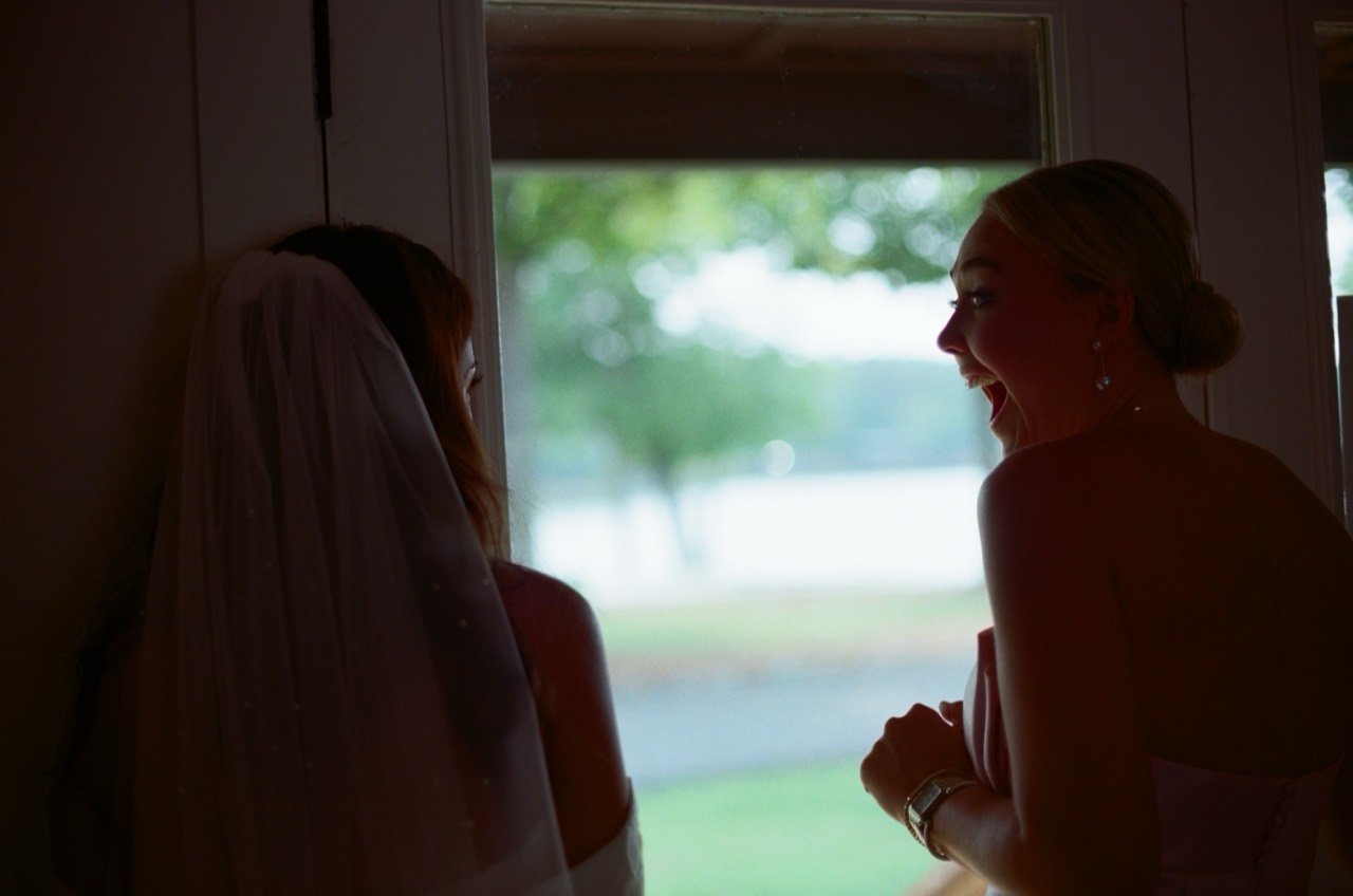 Brooklyn and a bridesmaid share a moment beside a window at New Water Farms, photographed on film.