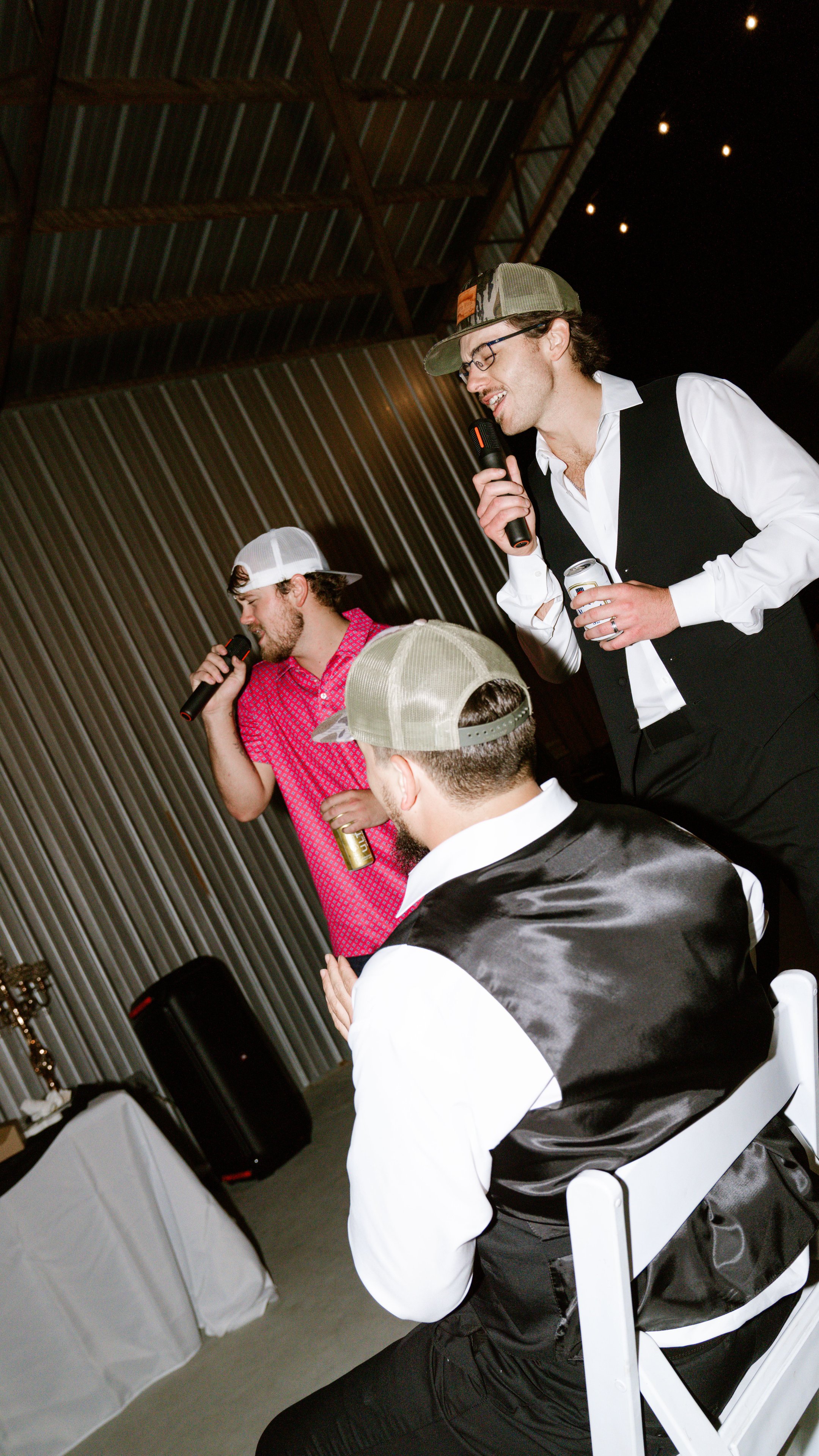 Two men singing into microphones while a third man in a vest stands in front of them at the reception.