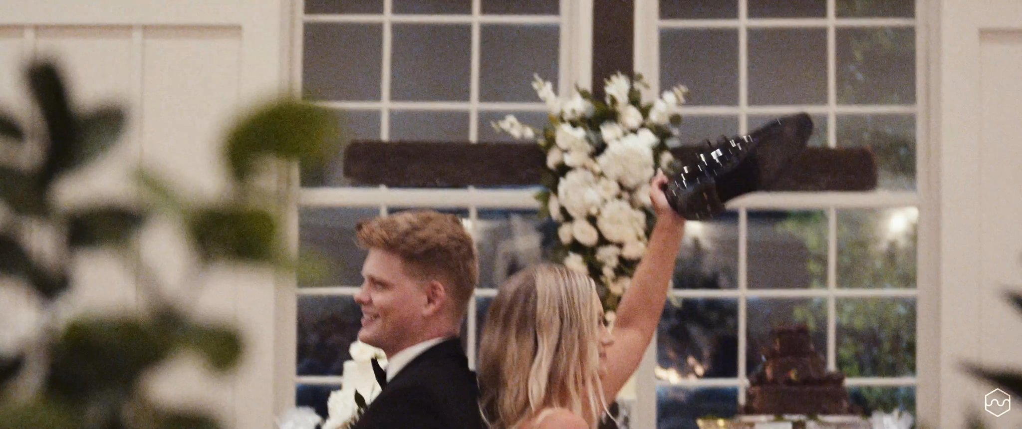 Madalyn raises her bouquet as she and Caleb enter their reception. Still from their Midsummer Productions wedding film.