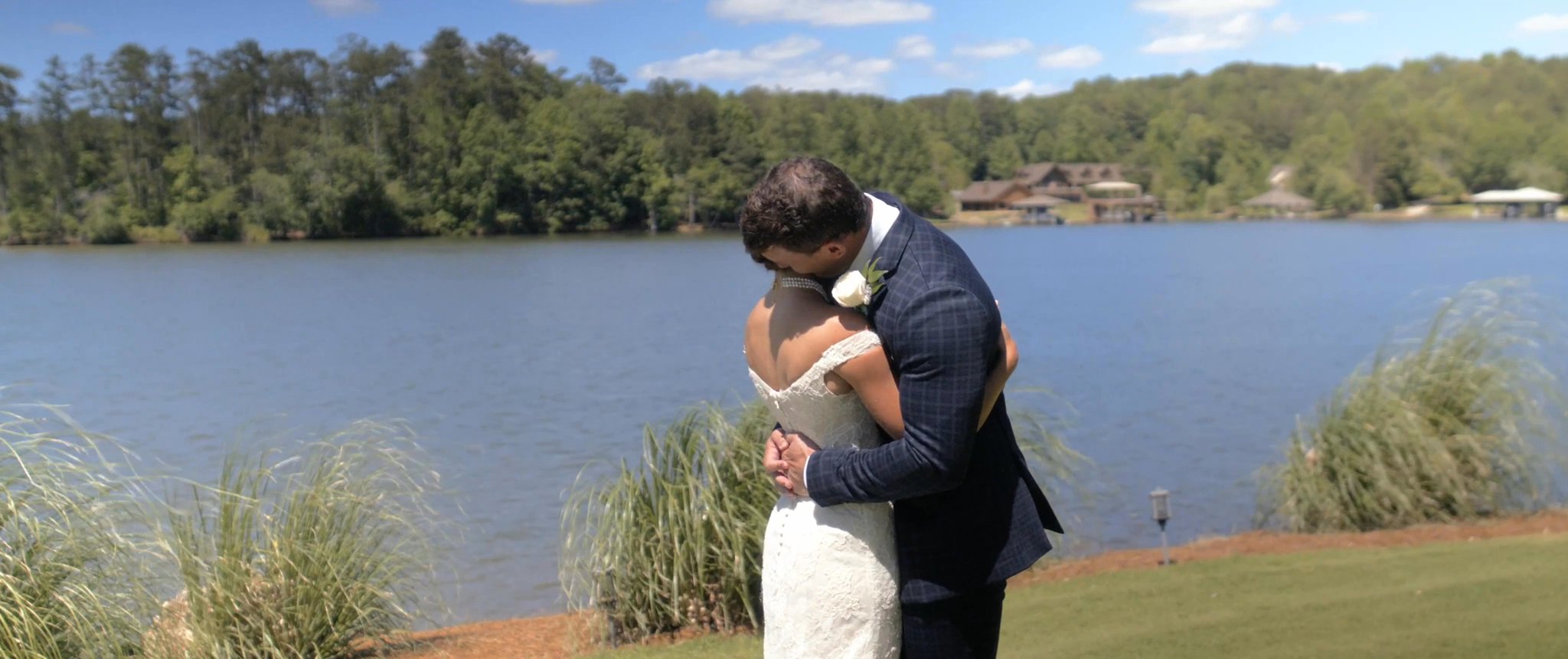 Julianna and Jake embrace beside the lake during their first look. Still from their Midsummer Productions wedding film.