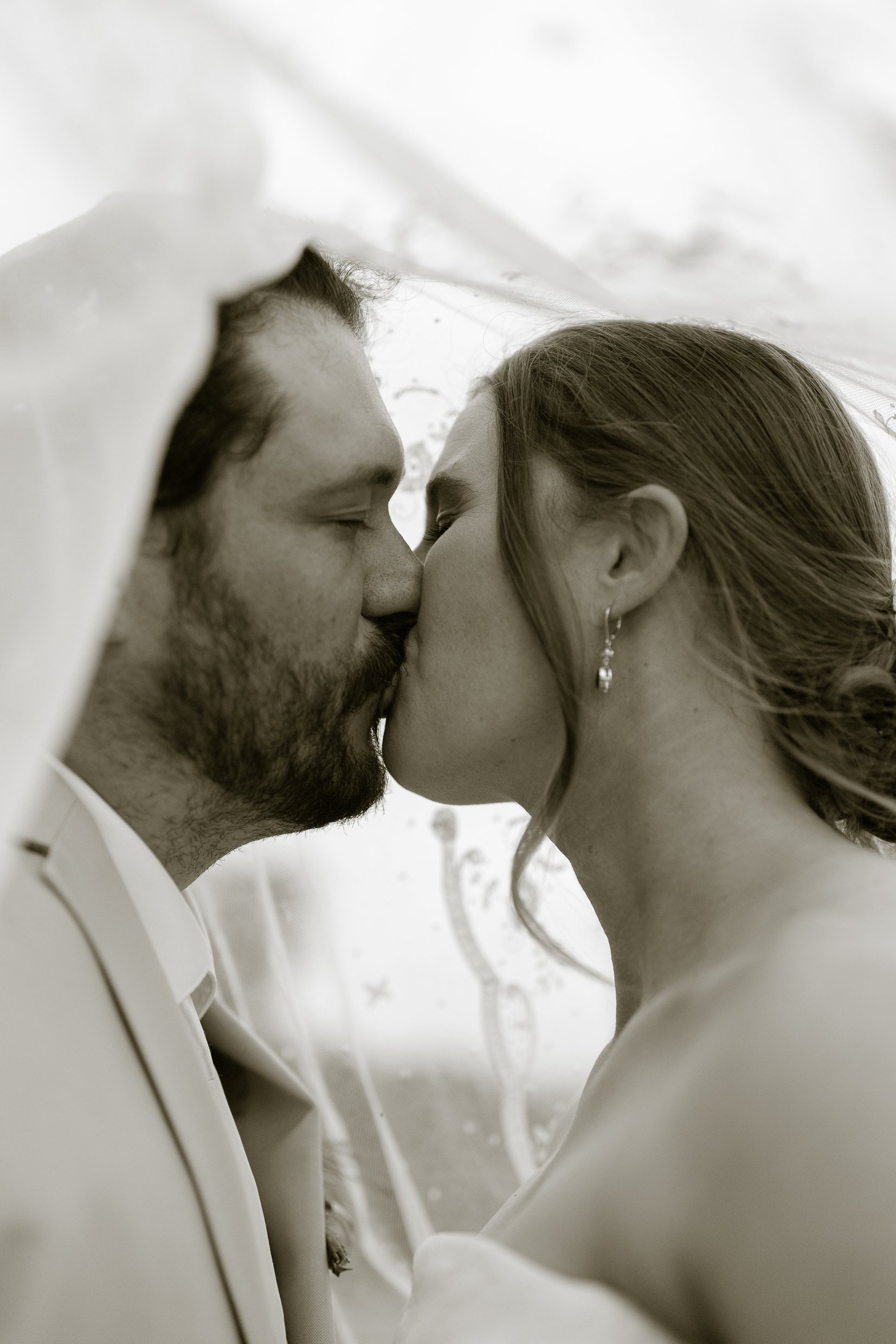 In a warm black and white tone, Dustin and Elizabeth kiss beneath her veil.