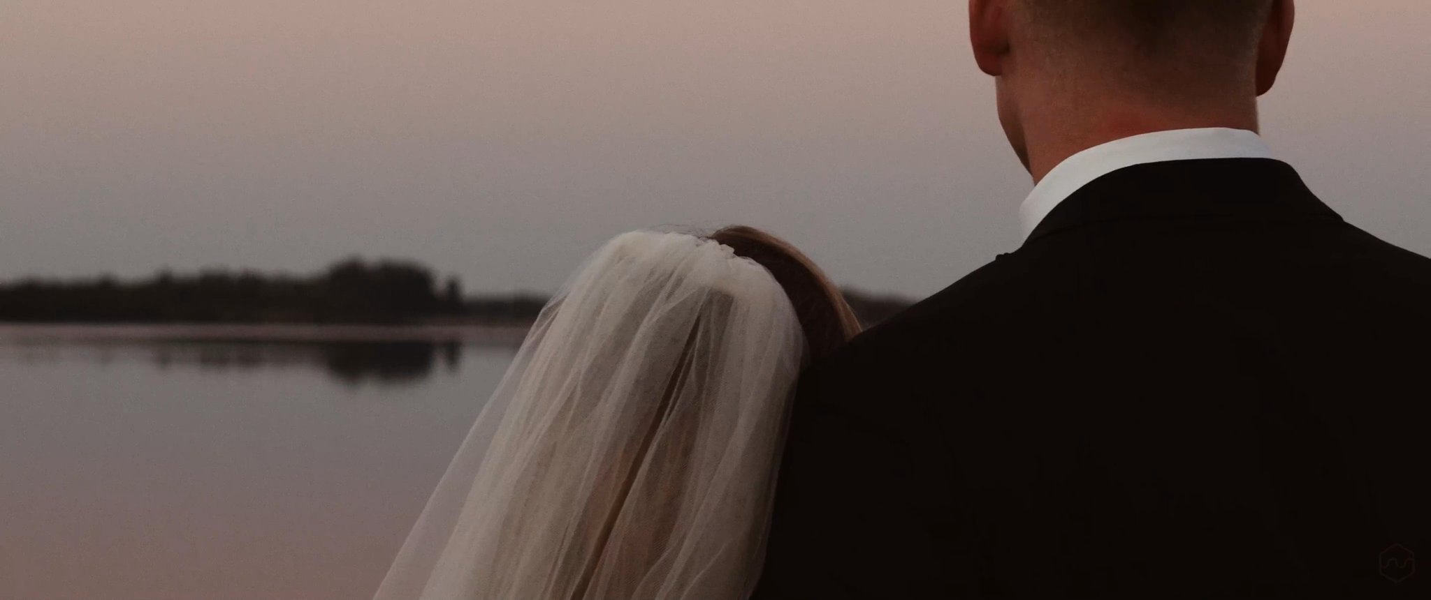 Madalyn and Caleb stand beside the water in the evening light. Still from their Midsummer Productions wedding film.