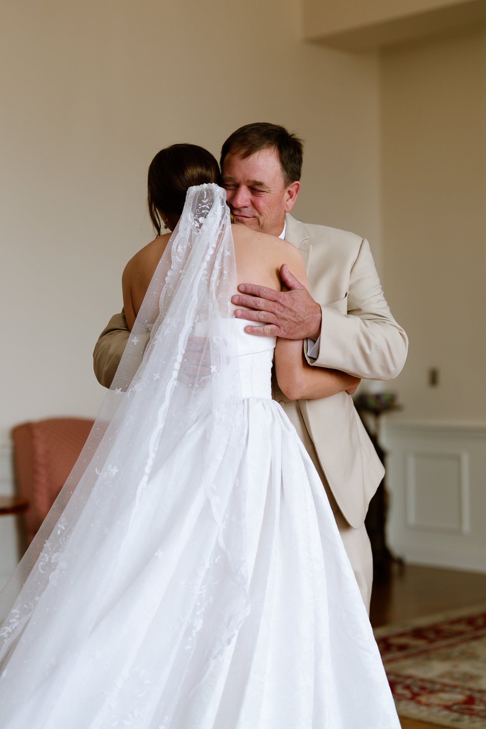 Elizabeth's father hugs her tight in a bright room, her long veil spilling down her back.
