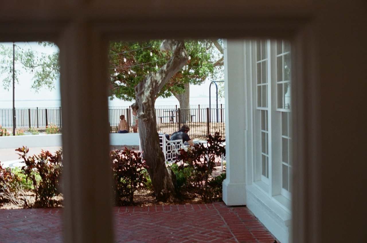 A view through the window to the waterfront courtyard at Jordan and Evan’s Tampa Yacht & Country Club wedding, photographed on film.