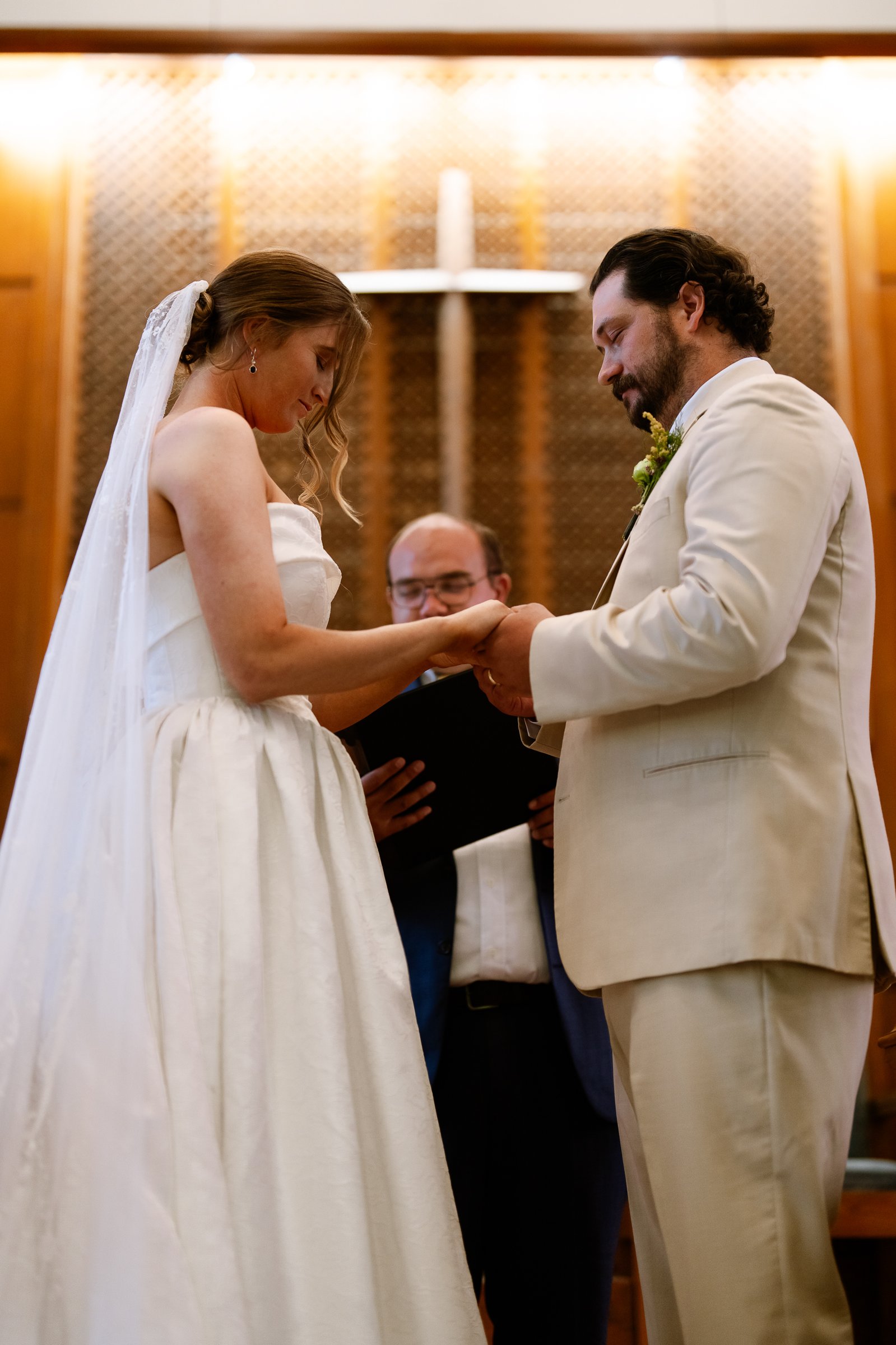 Elizabeth and Dustin hold hands in front of a wooden cross as the officiant looks on.