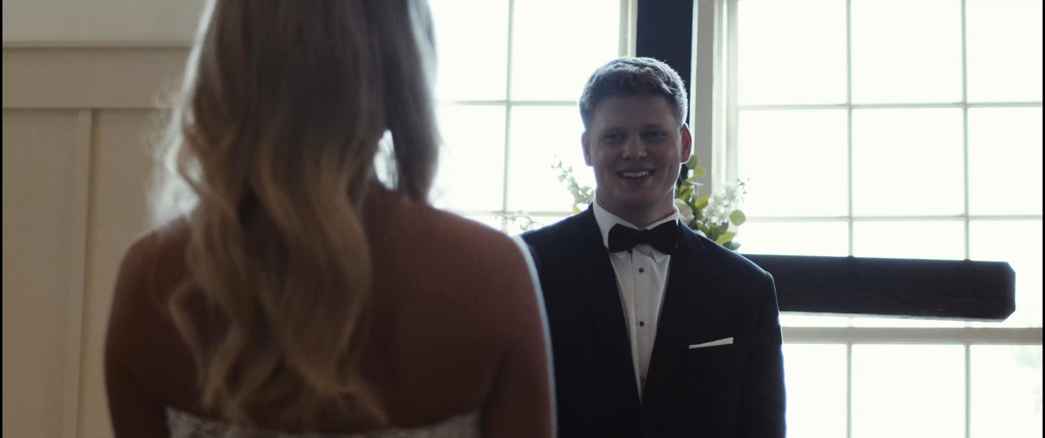 Caleb smiles as he sees Madalyn during their first look. Still from their Midsummer Productions wedding film.