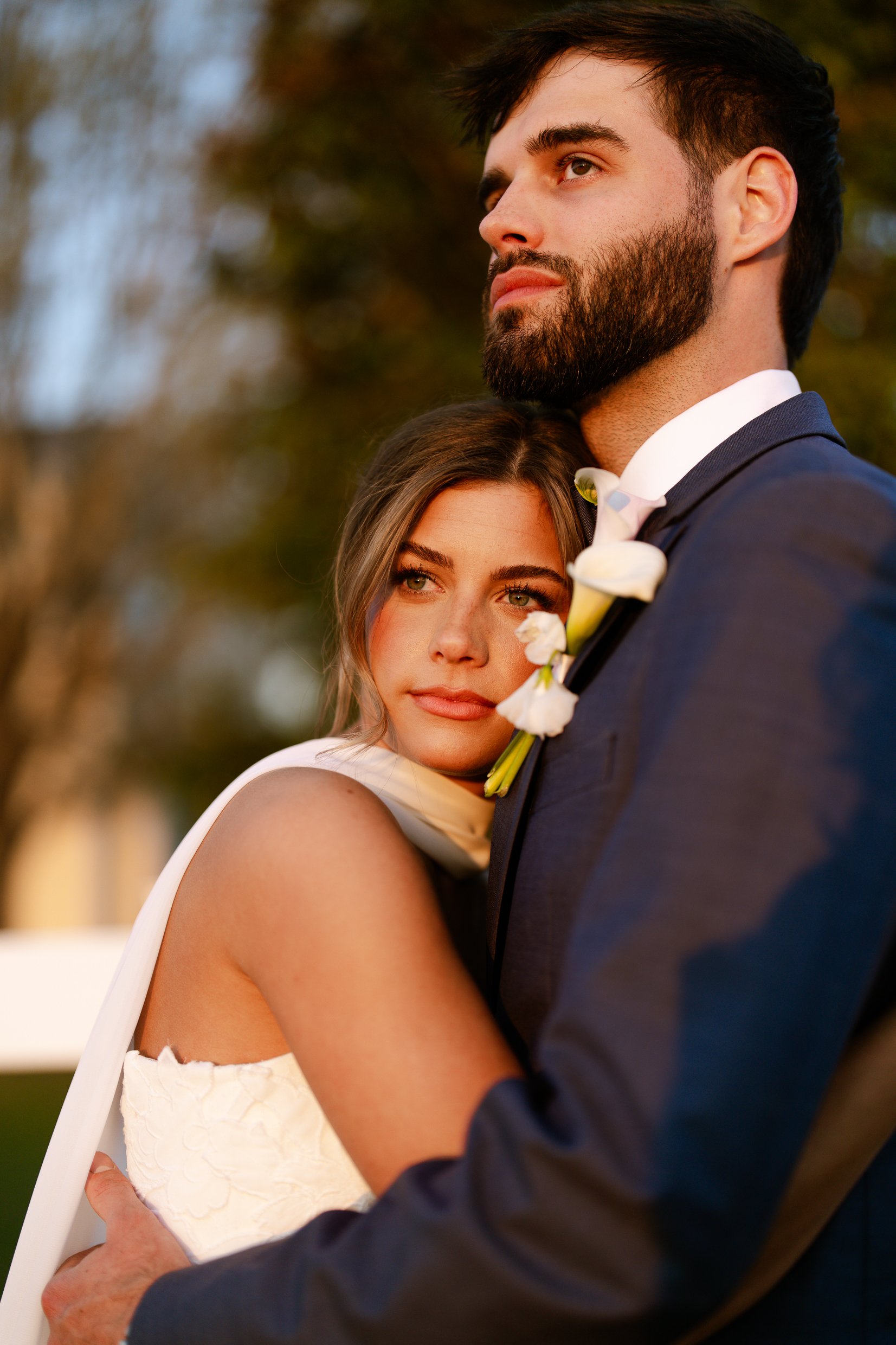 Joley rests her head against Matthew's chest while he looks off to the side, in warm low light.