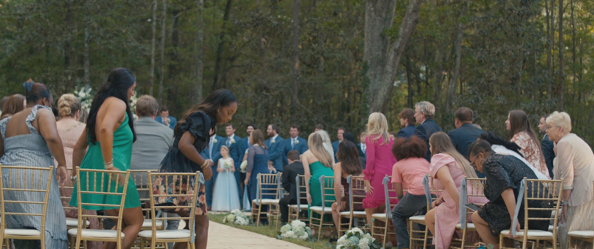A wide view of the outdoor ceremony with guests seated among the trees. Still from their Midsummer Productions wedding film.