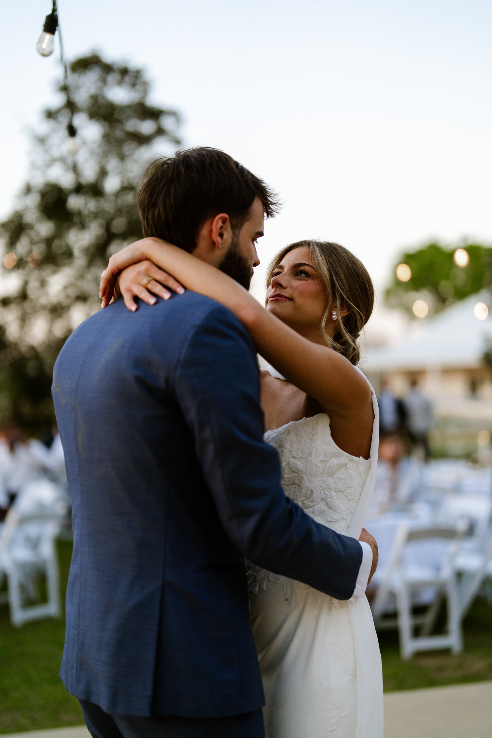 Joley has her arm around Matthew's neck at dusk, with tables and white chairs blurred behind them.