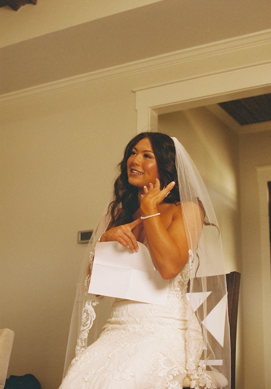 Raley seated in her lace wedding dress and veil, holding a handwritten letter at Dalrymple Farms, photographed on film.
