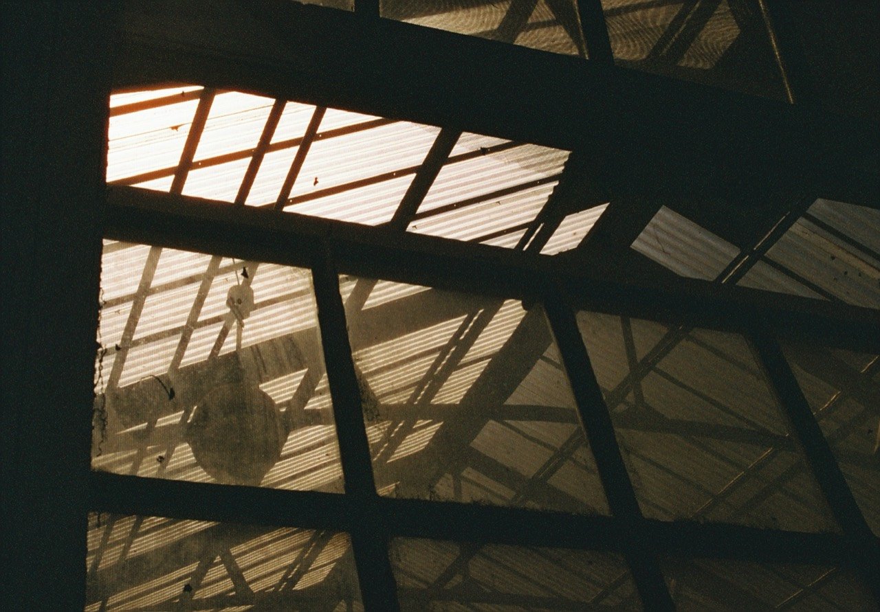 Sunlight through roof beams above a silhouetted chandelier at South Eden Plantation, photographed on film.