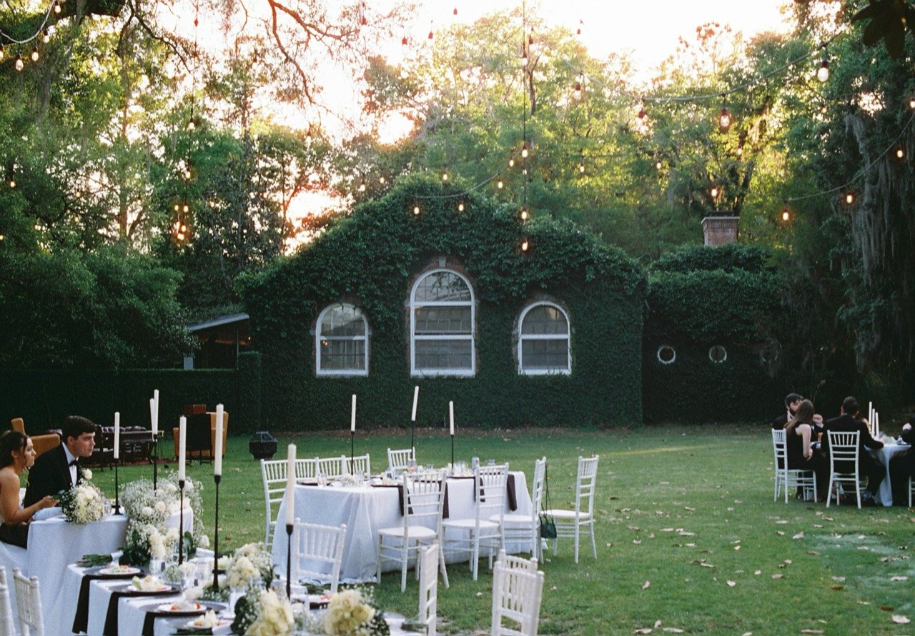 Outdoor dinner tables, white chairs and flowers beneath string lights at Emily and Timothy’s South Eden wedding, photographed on film.