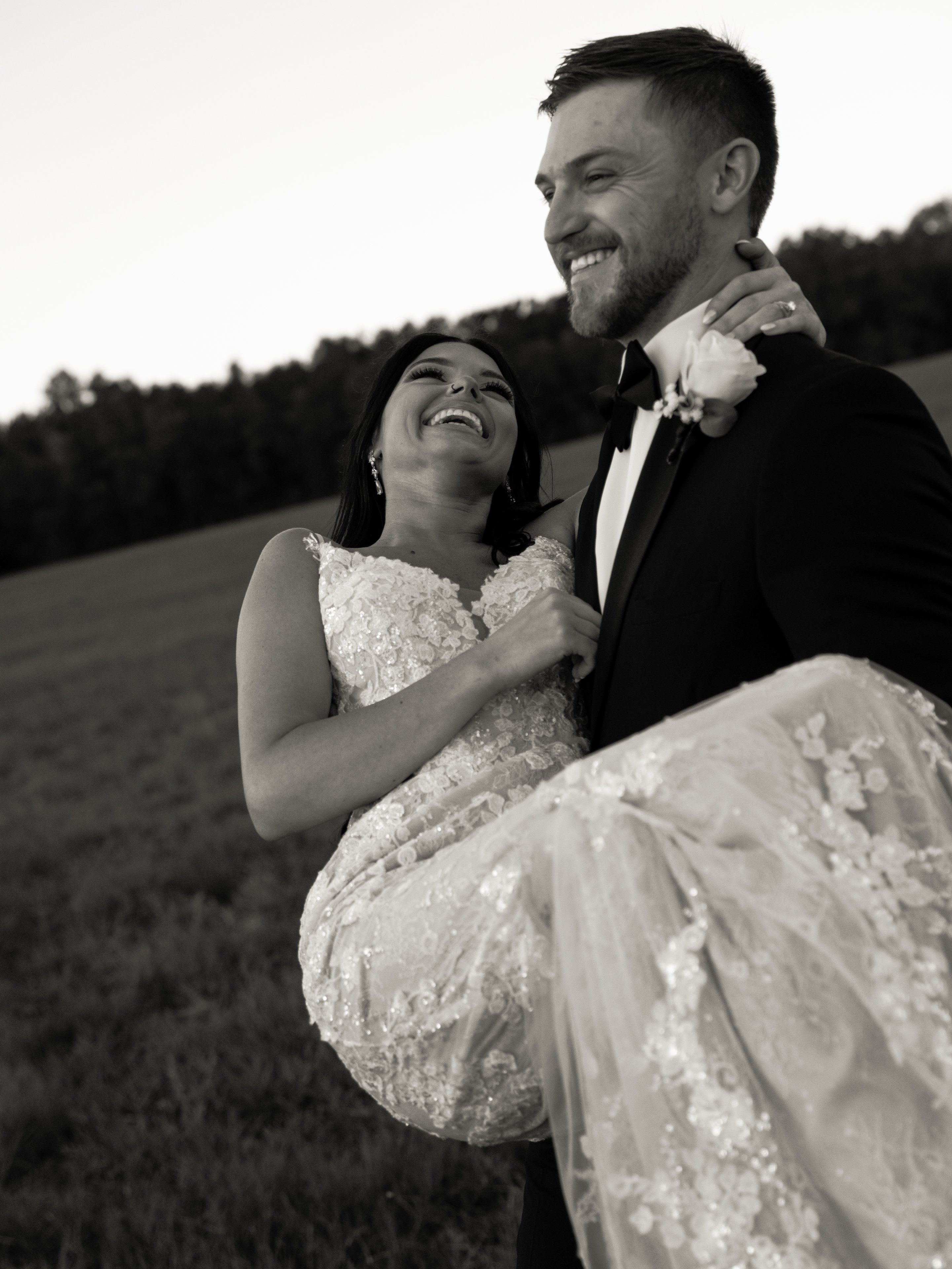 Corey carrying Kenadee in his arms in a field, both laughing.
