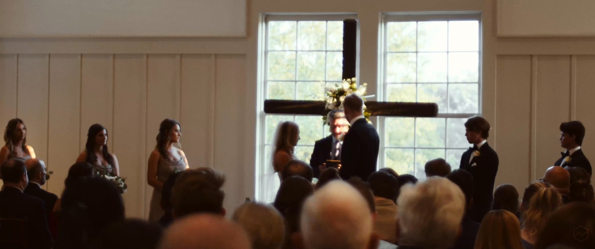 A wide view of Madalyn and Caleb’s ceremony in front of the flower-covered cross. Still from their Midsummer Productions wedding film.