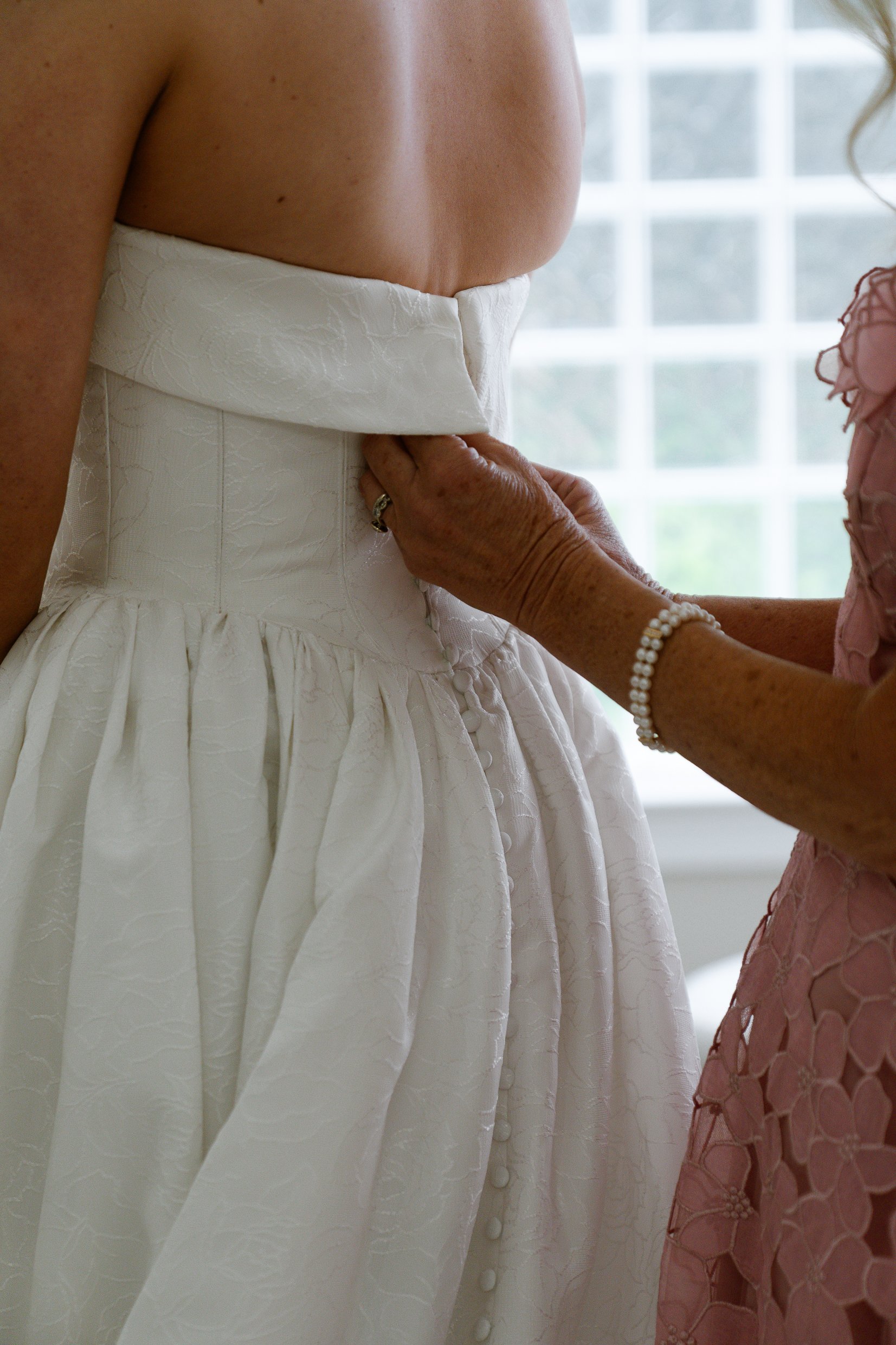 The back of Elizabeth's dress as a woman in a pink lace dress fastens the buttons below the folded top edge.