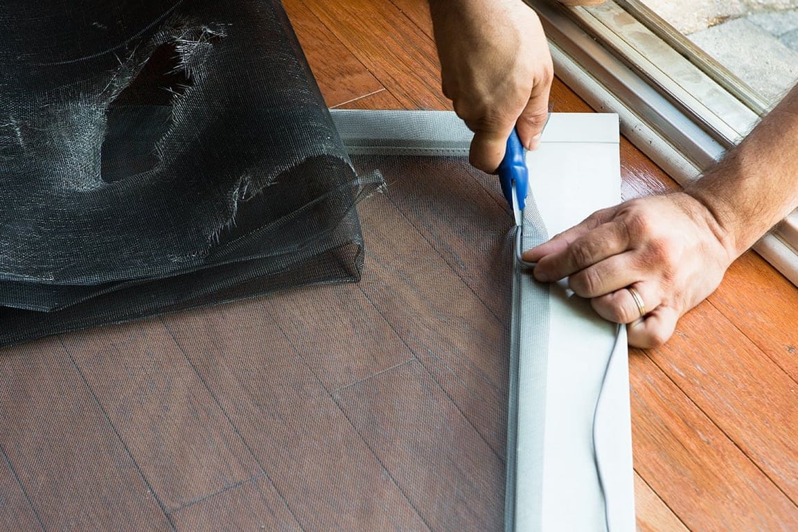 Professional window screen repair service in progress, cutting new screen material for installation in Greensboro