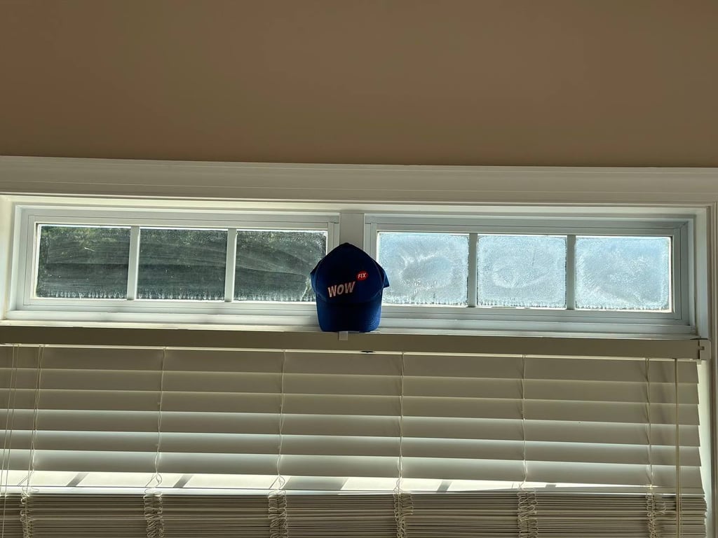Frosted basement window showing condensation issues with WOW FIX company hat, demonstrating common window repair needs in North Carolina