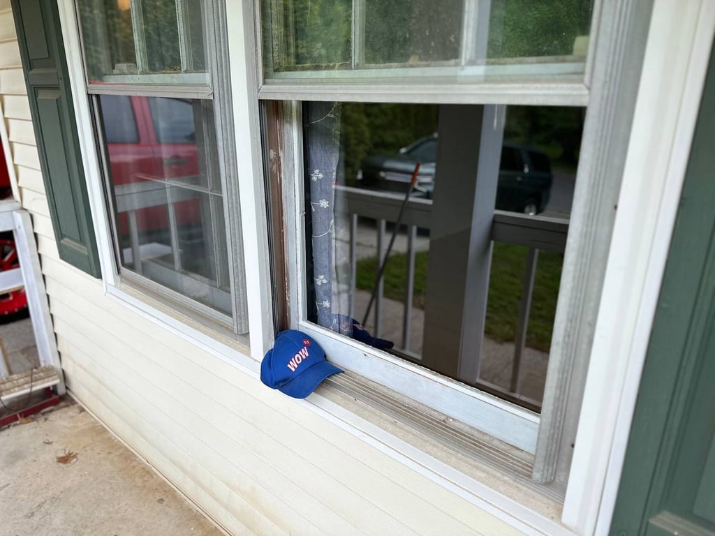Worn window frame with WOW company hat showing deterioration and aging, demonstrating need for professional window replacement