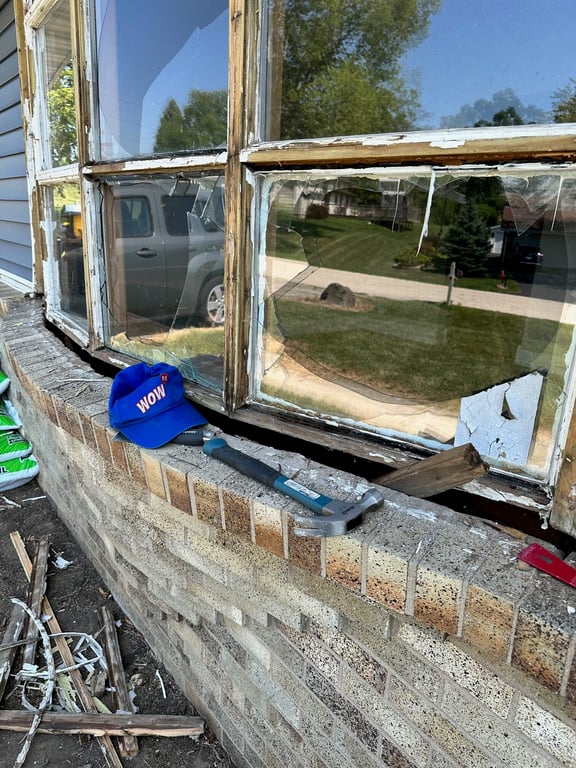 Severely damaged wooden window frame showing rot and deterioration, with repair tools on brick windowsill in Charlotte home