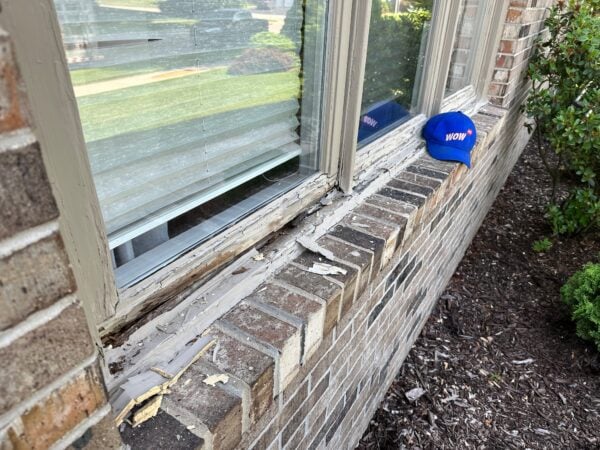 Severely damaged wooden window frame with rot and decay on brick home, demonstrating need for urgent window repair