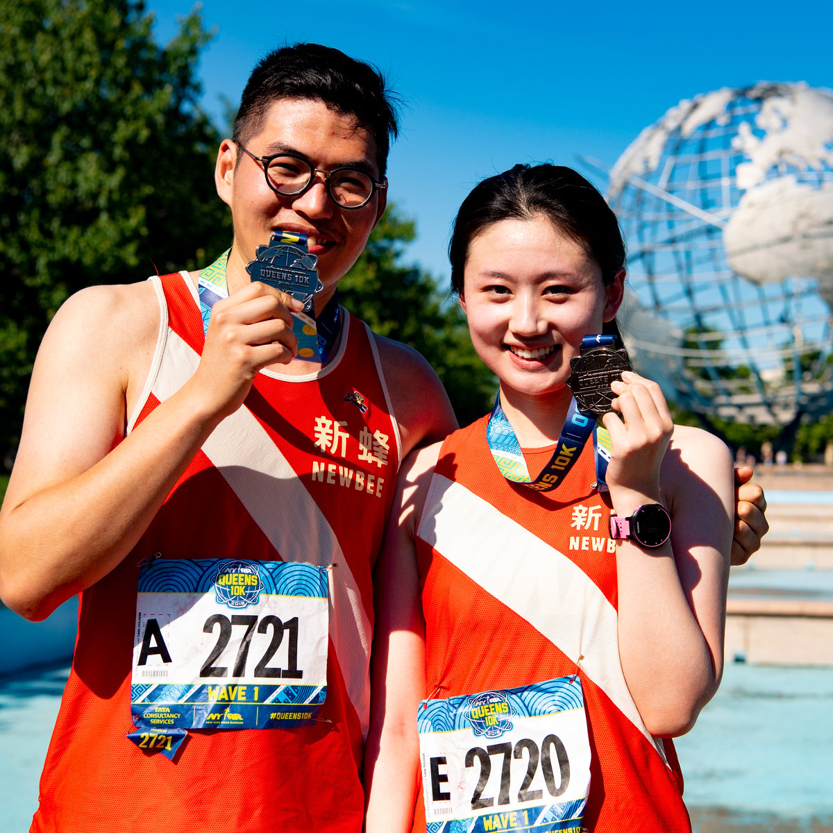 Runners holding their NYRR Queens 10K finisher medals in front of the Unisphere in Flushing Meadows Corona Park