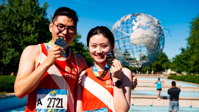 Runners holding their NYRR Queens 10K finisher medals in front of the Unisphere in Flushing Meadows Corona Park