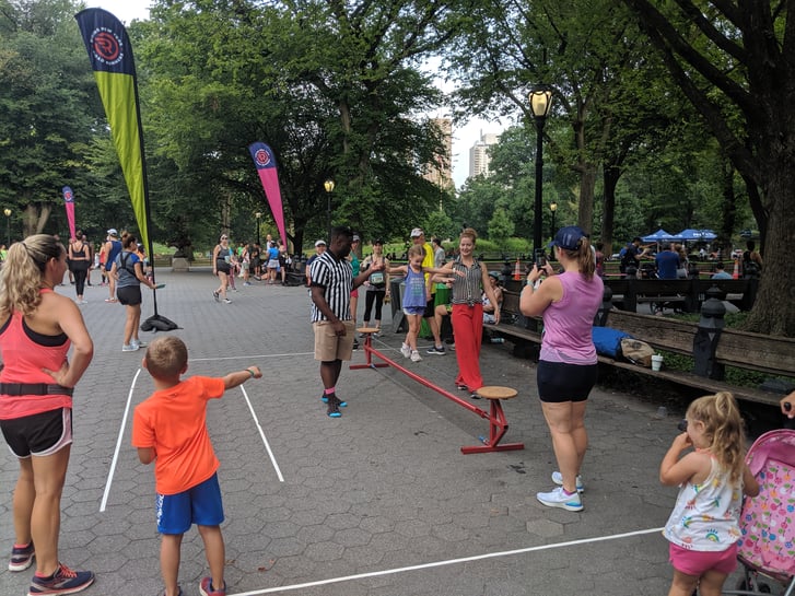 A child on a balance beam while her parents and other kids watch