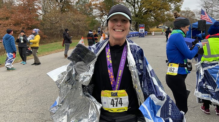 A woman after the NYRR 60K posing with her medal and souvenir backpack.