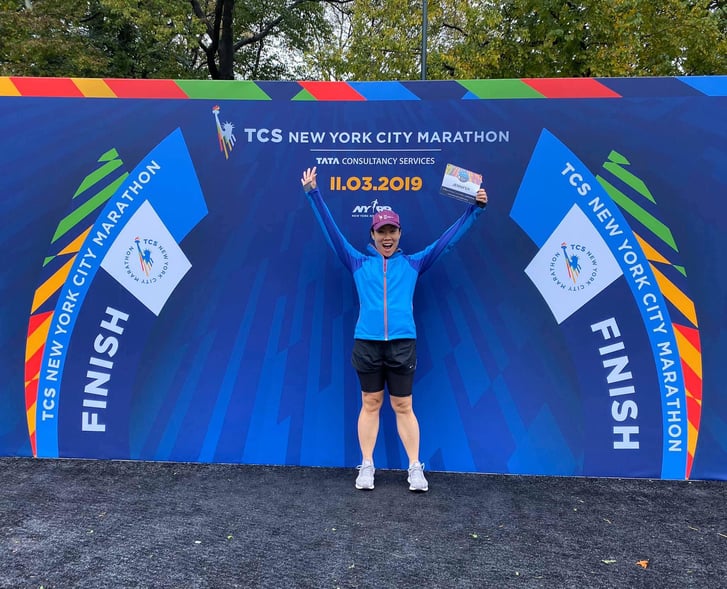 Jennifer Pyun holds her TCS NYC Marathon-Virtual 26.2M bib by the marathon finish line in Central Park.