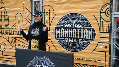 A runner posing in front of the NYRR Manhattan 7 Mile banner