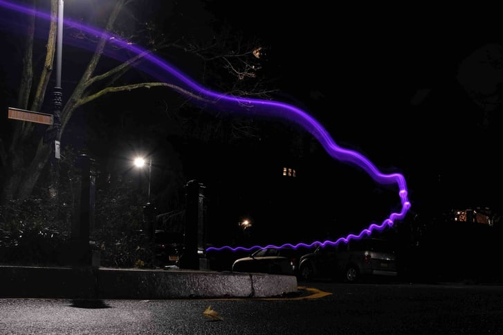 A nighttime street scene with a purple light streak moving across the frame
