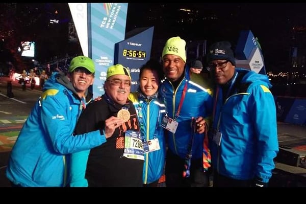 Randy Savitt after finishing TCS New York City Marathon holding medal and surrounded by volunteers