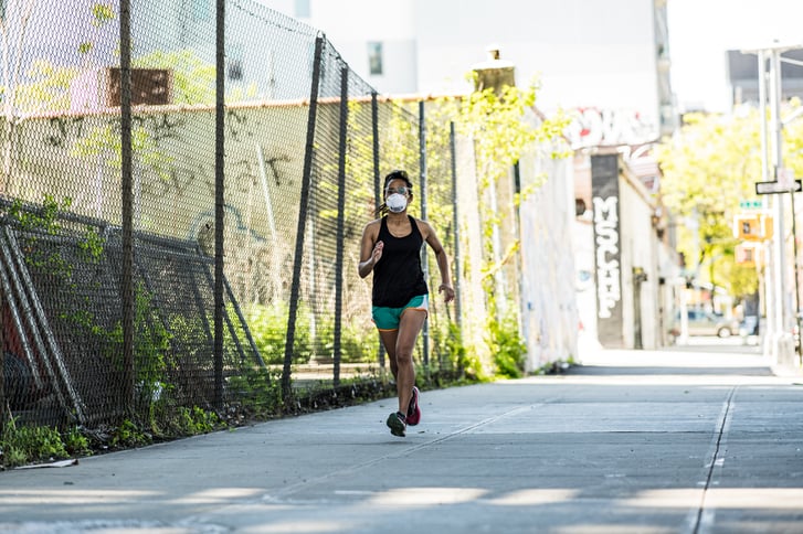 Woman runner on urban sidewalk wearing mask