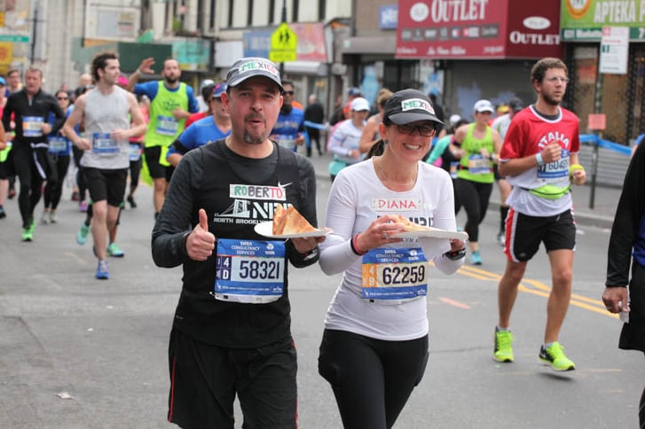 Two New York City Marathon runners holding slices of pizza while running