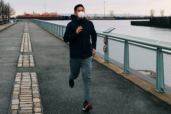 Leland Yu running in cityscape next to river wearing mask