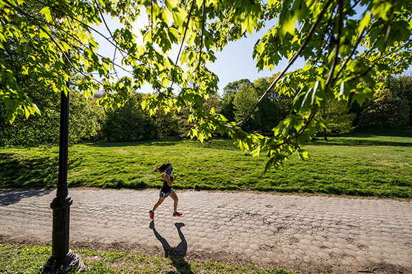 Masked woman running in Prospect Park landscape with greenery
