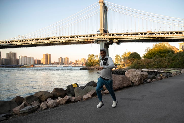 Man looks down at his watch while running on a path next to the water