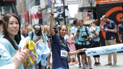 Des Linden holds the tape at a pop-up finish line in Times Square to celebrate Global Running Day.