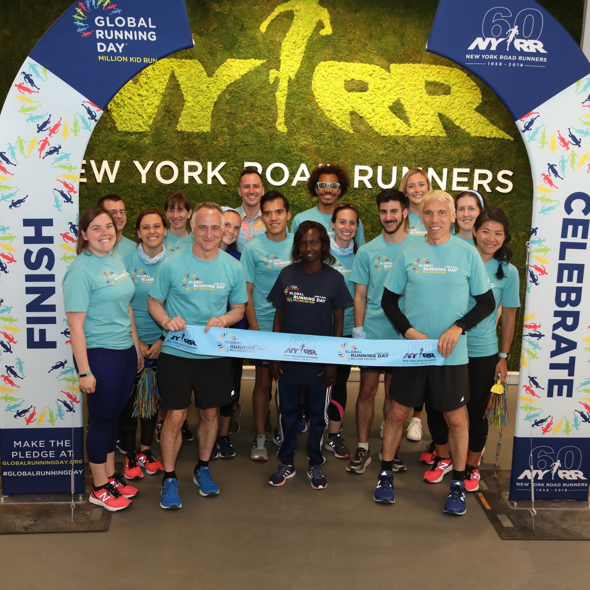 Three-time TCS New York City Marathon champion poses with Team NYRR staff after breaking a pop-up finish line tape in honor of Global Running Day at the NYRR RUNCenter.