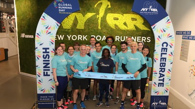Three-time TCS New York City Marathon champion poses with Team NYRR staff after breaking a pop-up finish line tape in honor of Global Running Day at the NYRR RUNCenter.