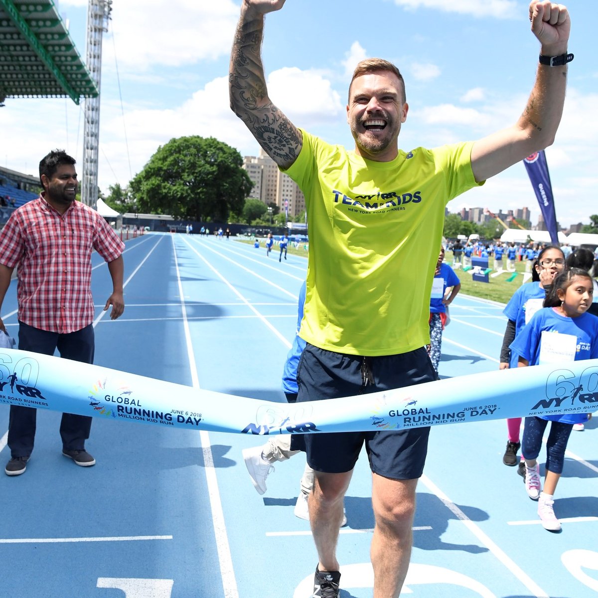 Team for Kids ambassador Nick Youngquest crosses a pop-up finish line tape at Icahn Stadium to celebrate Global Running Day.