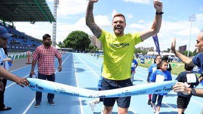 Team for Kids ambassador Nick Youngquest crosses a pop-up finish line tape at Icahn Stadium to celebrate Global Running Day.