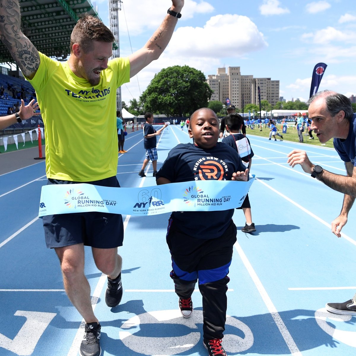Team for Kids ambassador Nick Younquest crosses a pop-up finish line tape to celebrate Global Running Day at Icahn Stadium with the Rising New York Road Runners.