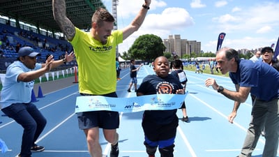 Team for Kids ambassador Nick Younquest crosses a pop-up finish line tape to celebrate Global Running Day at Icahn Stadium with the Rising New York Road Runners.