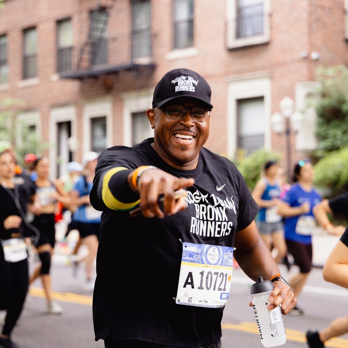 A runner is a Boogie Down Bronx runners t-shirt smiles and points at the camera during the RBC Brooklyn Half